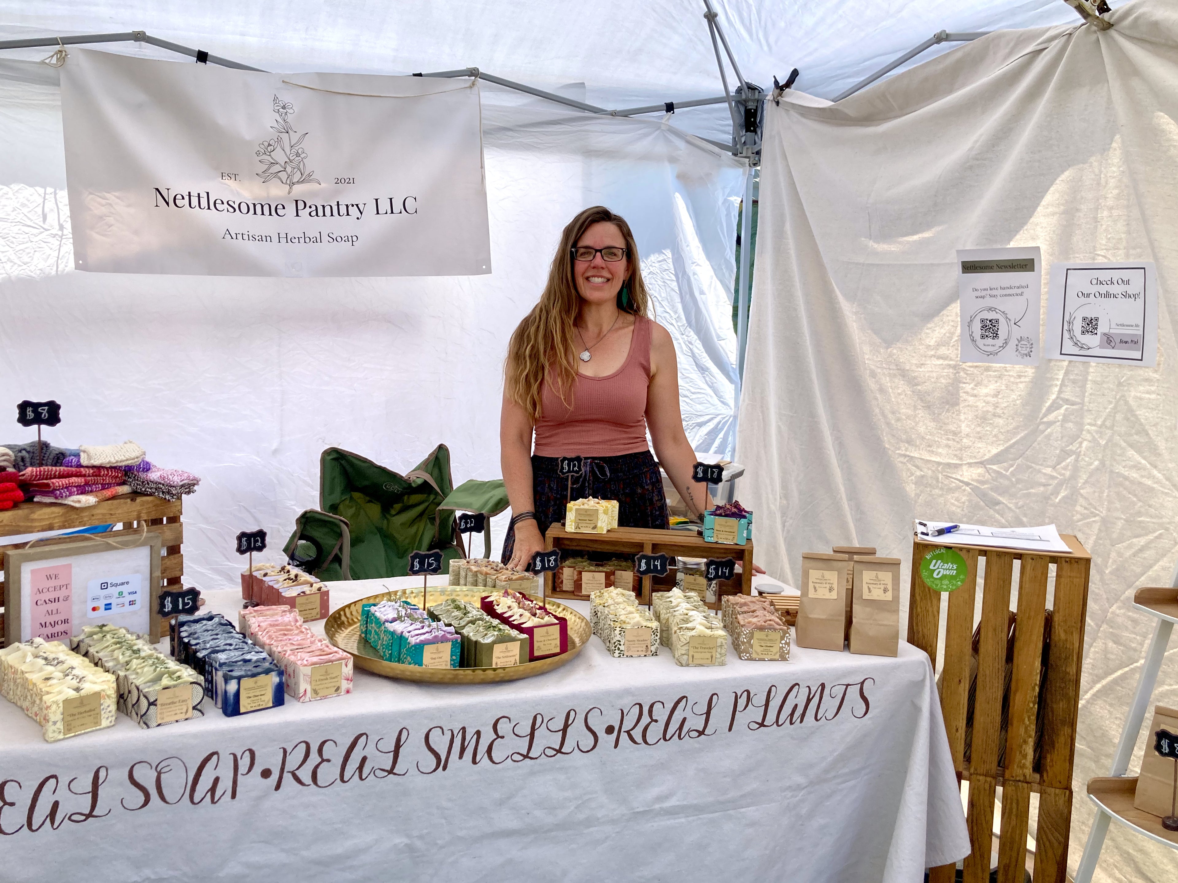 Woman standing behind a table with soap products at a Nettlesome Pantry LLC booth.