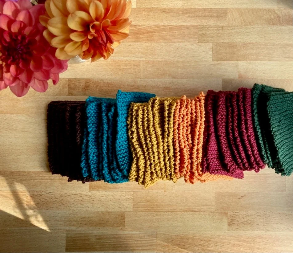 Colorful knitted dishcloths on a wooden surface with flowers in the background